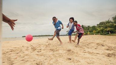 A boy kicks the ball hard to score a goal, in a game of soccer on the beach.