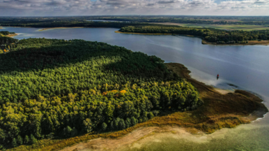 A breathtaking aerial view of a lush forest bordering a serene lake under a partly cloudy sky