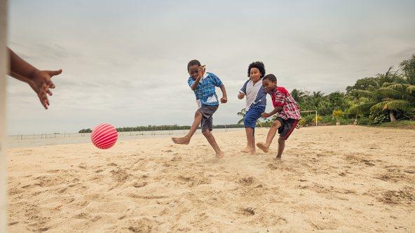 A boy kicks the ball hard to score a goal, in a game of soccer on the beach.