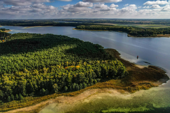 A breathtaking aerial view of a lush forest bordering a serene lake under a partly cloudy sky