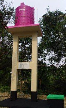 Elevated pink water tank on a tall cream-colored support structure surrounded by trees.