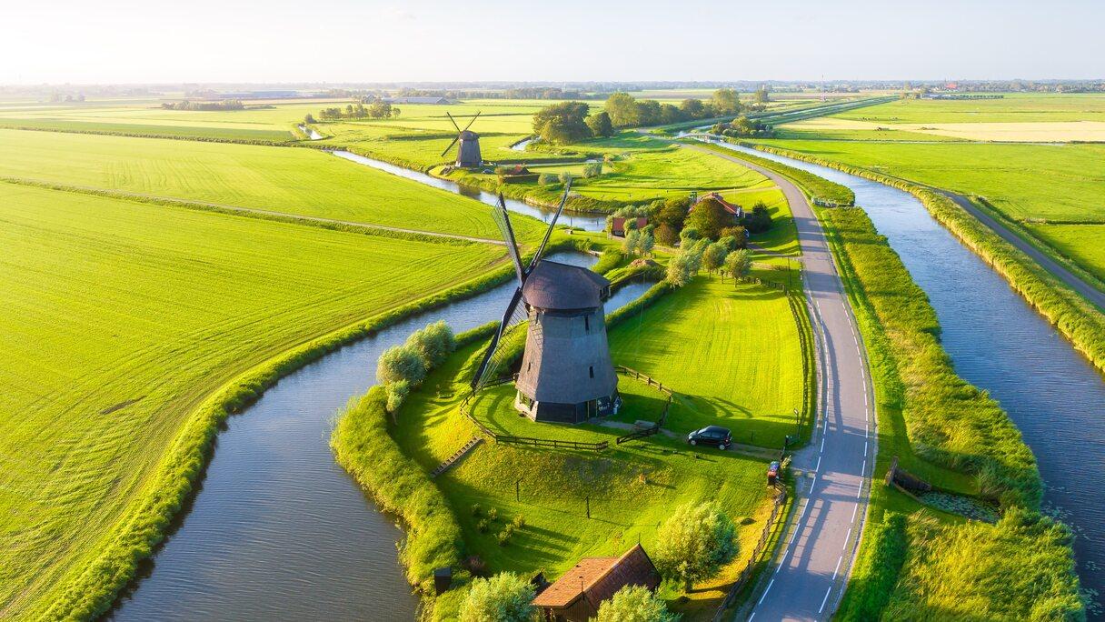 A drone view of windmills in Holland. Windmills on the banks of canals. Agricultural fields and pastures. Summer landscape in The Netherlands